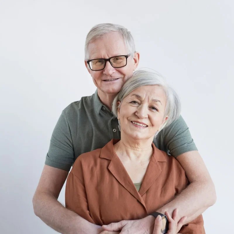 vertical-portrait-loving-senior-couple-embracing-looking-camera-while-standing-against-white-background
